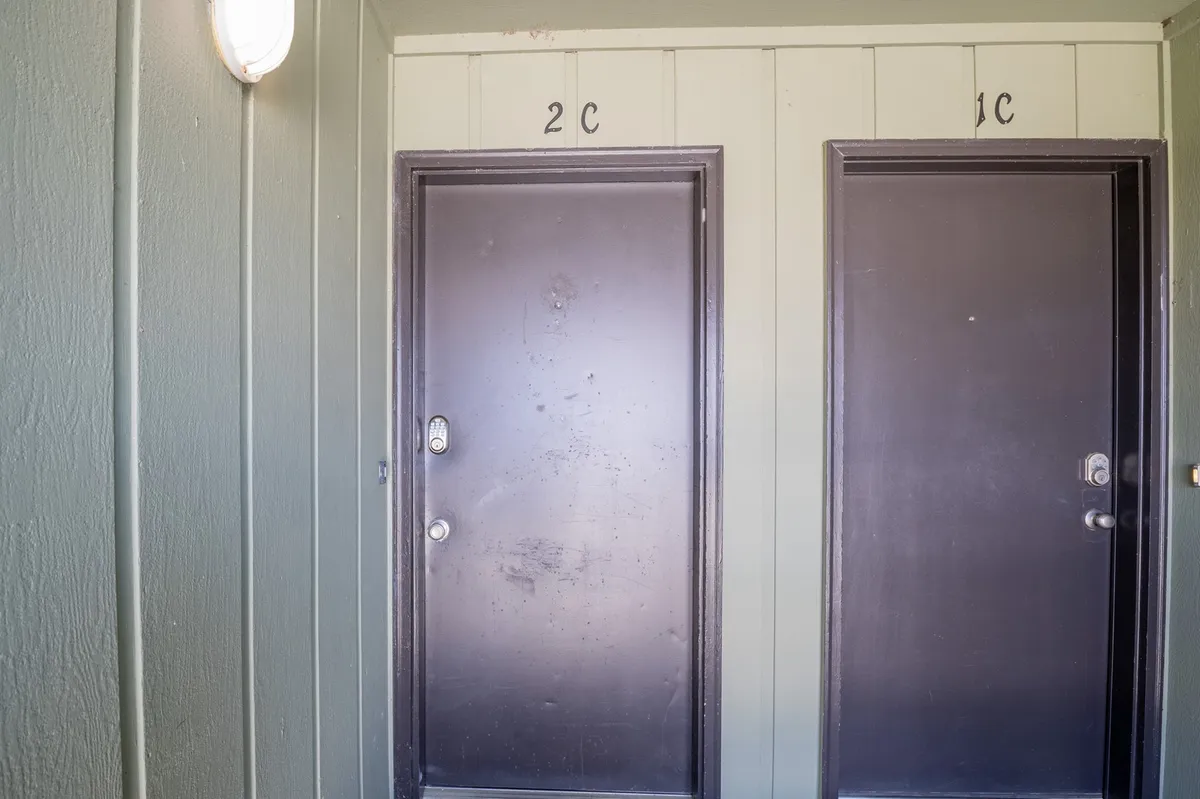 A view of two exterior doors labeled 1C and 2C under a dim lighting fixture, hinting at the entrance or arrival point for guests. The scene suggests a sense of anticipation, arrival, and gathering, appropriate for welcoming groups.