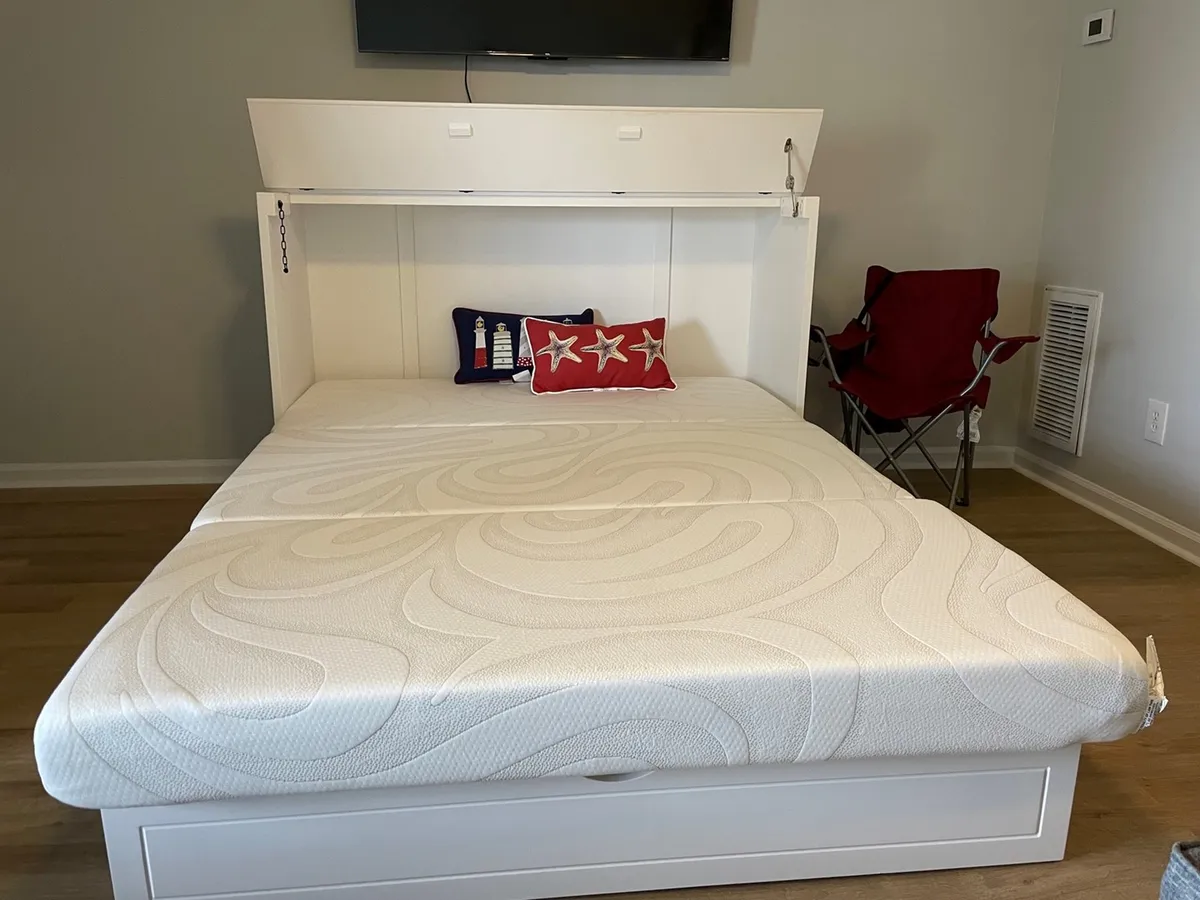 A cleverly designed Murphy bed is tucked into a credenza, positioned near a television and flanked by decorative pillows. The space feels inviting and versatile, ready to transform from a living area to an extra sleeping space as needed.