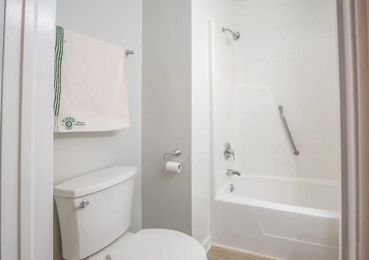 A clean, functional bathroom with a toilet, bathtub, towel, and grab bar. The simple design conveys ease of use and accessibility, supporting both comfort and practicality for all guests.