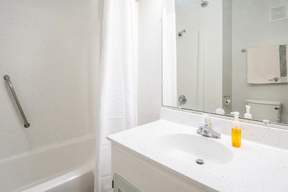 A serene, well-appointed bathroom featuring a modern sink, bathtub, mirror, soap dispenser, and a neatly folded towel, evoking a spa-like atmosphere. The space is bright and spotless, suggesting attention to cleanliness and comfort.