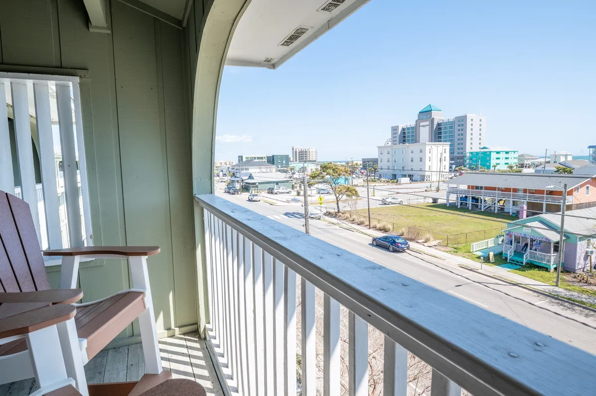 This image captures a private balcony with classic rocking chairs overlooking the city. The inviting setting is perfect for enjoying morning coffee or an evening cocktail while soaking in the vibrant downtown atmosphere. The presence of the balcony railing and the lively city view reinforces the connection with Carolina Beach’s energetic locale.