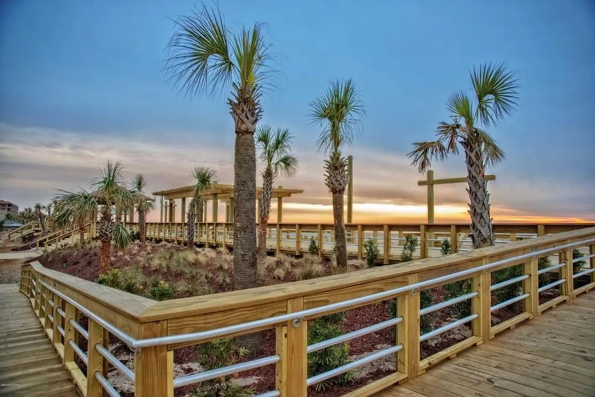 A serene exterior shot featuring a palm-lined boardwalk at sunset, with a viewing platform overlooking the water. The tranquil setting hints at evening strolls, photography opportunities, and relaxed gatherings for families seeking quieter moments during their stay.