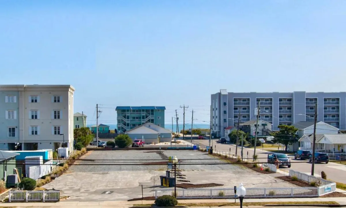 A sweeping exterior view features the beach and surrounding buildings, creating a sense of place and adventure. The visible parking area and road hint at walkable access to attractions, while the ocean backdrop highlights the proximity to waterfront activities, fireworks, and romantic strolls along the shore.