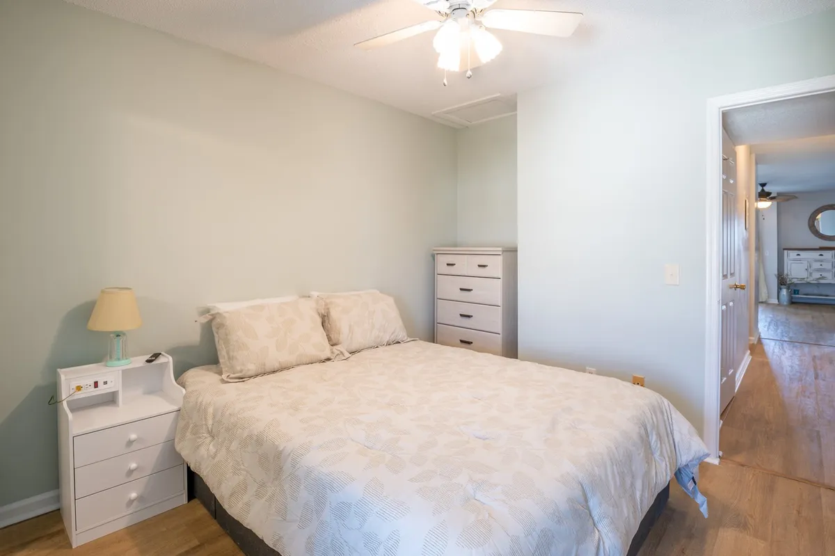 A tranquil bedroom with a neatly made bed, nightstand, and dresser, illuminated by natural morning light. The space exudes calm, ideal for restful solo retreats.